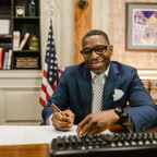 Smiling lawyer writing documents in a well-decorated office setting with legal books and US flag.